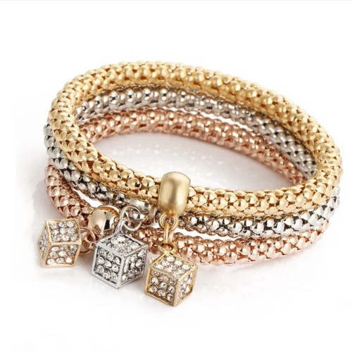 Three interconnected bracelets in gold, silver, and rose gold, each with a dangling crystal cube charm.